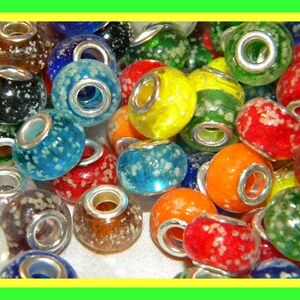 May include: A collection of colorful glass beads with silver metal accents. The beads are speckled with white flecks and have a variety of colors, including red, orange, yellow, green, blue, and black.