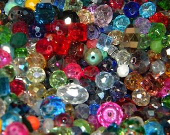 May include: A large assortment of colorful glass beads in various shapes and sizes. The beads are a mix of clear, opaque, and iridescent colors, including red, blue, green, and purple.