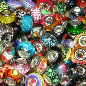May include: A collection of colorful glass beads with silver-toned metal cores. The beads feature various designs, including glitter, floral patterns, and abstract shapes. Colors include blue, green, red, orange, and yellow. These beads are suitable for jewelry making.