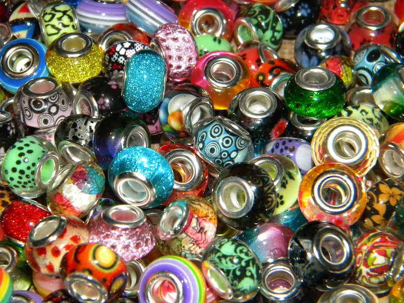 May include: A collection of colorful glass beads with silver-toned metal cores. The beads feature various designs, including glitter, floral patterns, and abstract shapes. Colors include blue, green, red, orange, and yellow. These beads are suitable for jewelry making.