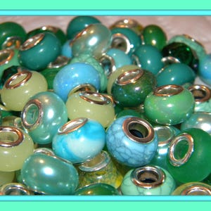 May include: A collection of round beads in various shades of green, teal, and blue, each featuring a central silver-toned metal core. The beads display diverse finishes, including opaque, translucent, pearlescent, and cracked textures.