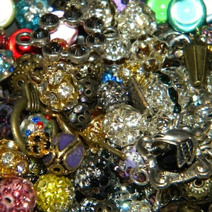 May include: A close-up of a variety of colorful beads and charms, including silver, gold, blue, green, red, and purple. The beads are arranged in a random pattern and some are strung together on a chain.