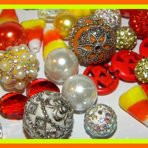 May include: Assortment of Halloween themed beads in orange, red, white, and yellow. The beads are made of glass, plastic, and metal. Some beads are shaped like candy corn.