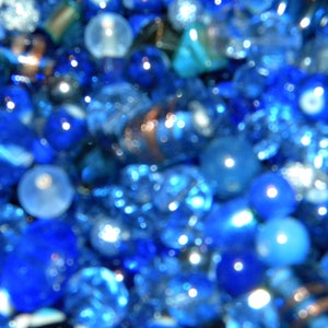 Peut inclure: Gros plan sur une collection de perles de verre bleues, certaines avec une finition claire et iris&eacute;e. Les perles sont floues, cr&eacute;ant un effet abstrait flou.