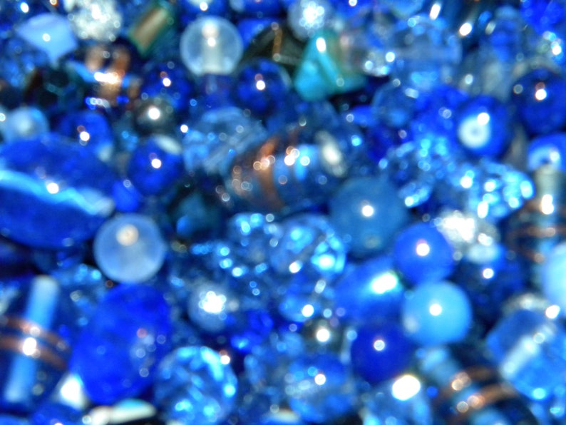 Peut inclure: Gros plan sur une collection de perles de verre bleues, certaines avec une finition claire et iris&eacute;e. Les perles sont floues, cr&eacute;ant un effet abstrait flou.