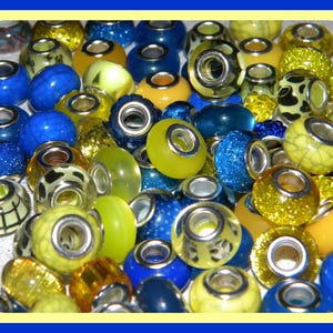 May include: A collection of yellow and blue glass beads with silver accents. The beads are various shapes and sizes, including round, oval, and square.