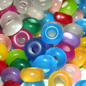 May include: A collection of round, smooth, translucent beads in a variety of vibrant colors including red, blue, green, yellow, purple, pink, and white. Each bead features a central hole, creating a donut-like shape with a glossy finish.