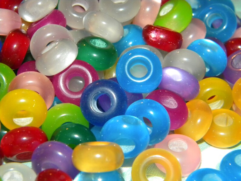 May include: A collection of round, smooth, translucent beads in a variety of vibrant colors including red, blue, green, yellow, purple, pink, and white. Each bead features a central hole, creating a donut-like shape with a glossy finish.