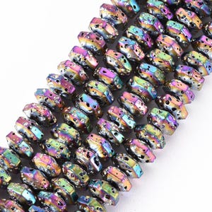 May include: A strand of iridescent, multi-colored beads with a metallic finish. Each bead features a rough, porous texture with small indentations and a flattened, irregular shape, displaying shifting hues of purple, green, blue, and gold.