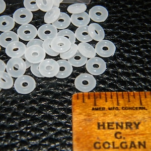 May include: A pile of white plastic spacer beads. The beads are approximately 1.2 cm in diameter and have a hole in the centre.