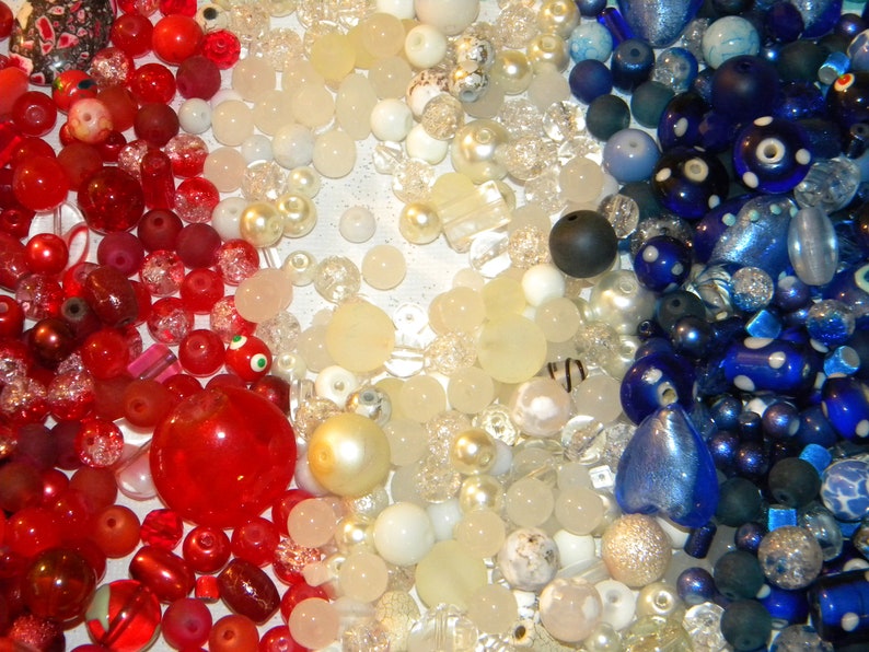 Peut inclure: Une collection de perles rouges, blanches et bleues. Les perles sont de formes et de tailles vari&eacute;es, notamment rondes, carr&eacute;es et en forme de c&oelig;ur. Certaines perles sont transparentes, tandis que d'autres sont opaques.