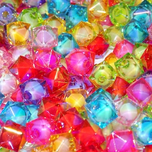 May include: A collection of translucent, multi-faceted cube-shaped beads in vibrant shades of red, blue, pink, yellow, and green. Each bead features a clear, glossy finish with a central hole, creating a dense, colorful pile of geometric shapes.