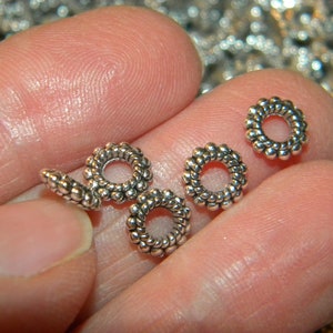 May include: Close-up of four silver metal bead spacers with a textured, twisted design. The spacers are round with a small hole in the center.