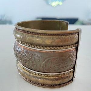 Puede incluir: Pulsera de pu&ntilde;o ancha con acabado de lat&oacute;n antiguo. La pulsera presenta tres bandas apiladas con intrincados patrones florales en relieve y trabajos decorativos en metal. El pu&ntilde;o mide aproximadamente 6,35 cm de ancho.