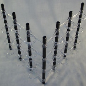 May include: A clear plastic display stand with black rods and circular holders. The stand is designed to hold and display multiple items, such as jewelry or small objects.