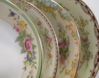 May include: A close-up of four antique porcelain plates with floral and ornate designs. Each plate features a different border pattern, including pink roses, gold accents, and a green trim. The plates are arranged in a slightly overlapping manner.
