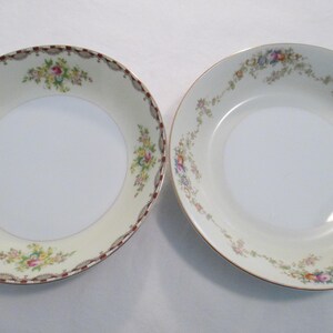 May include: Two vintage porcelain bowls with floral patterns. One bowl features a cream-coloured rim with a brown and gold border, the other has a gold rim. Both bowls have a white centre and are decorated with colourful flowers.