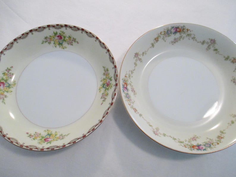 May include: Two vintage porcelain bowls with floral patterns. One bowl features a cream-coloured rim with a brown and gold border, the other has a gold rim. Both bowls have a white centre and are decorated with colourful flowers.