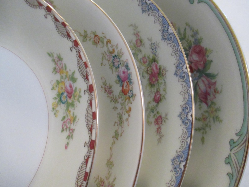 May include: Close-up of four decorative plates with floral patterns. The plates have a cream background and gold rims. Each plate features a different floral design in pink, blue, yellow, and green.