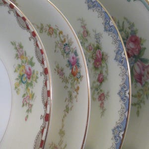 May include: Close-up of four antique porcelain plates. Each plate has a different floral design with gold trim. The plates have a cream background with pink, blue, and yellow flowers.