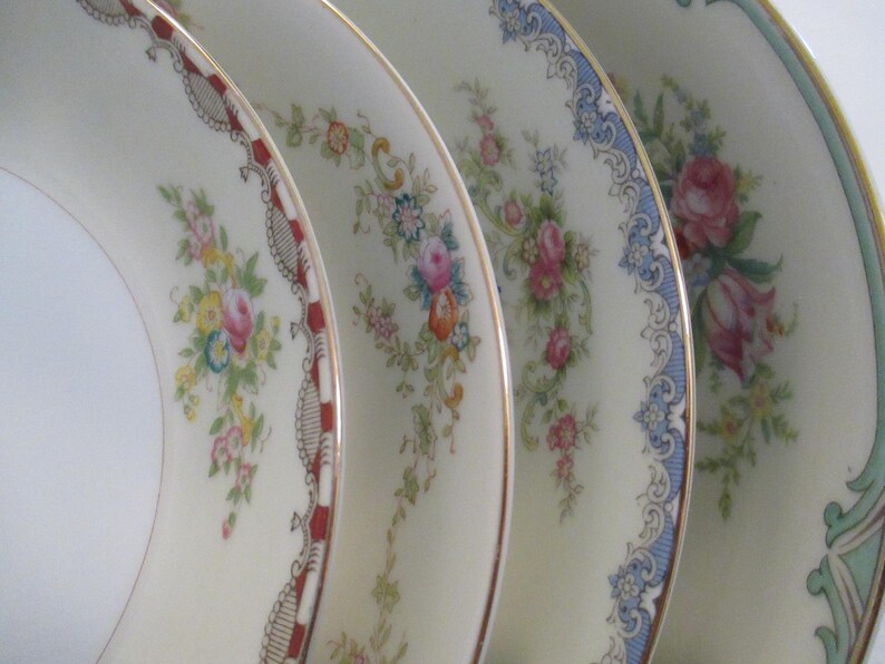 May include: Close-up of four antique porcelain plates. Each plate has a different floral design with gold trim. The plates have a cream background with pink, blue, and yellow flowers.