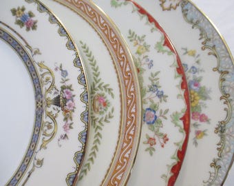 Può includere: Una collezione di piatti in porcellana fine con intricati disegni floreali e ornamentali. Ogni piatto presenta un diverso motivo a bordo, con accenti blu, oro, rossi e arancioni. I piatti mostrano una varietà di composizioni floreali ed elementi decorativi.