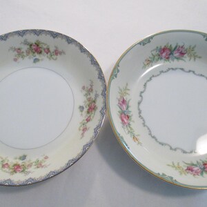 May include: Two white porcelain bowls with floral patterns. One has a blue and gold rim with pink and blue flowers. The other has a gold rim with pink flowers and a green border. Both bowls have a white centre.