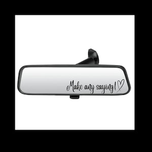 May include: A rectangular vehicle rearview mirror with a black frame and mounting arm. The reflective surface features black cursive text that reads Make any saying! followed by a hand-drawn heart outline on the right side of the mirror.