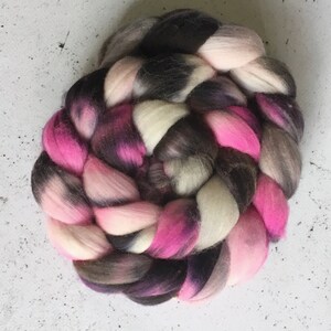 Könnte beinhalten: Ein geflochtenes Garnbündel in den Farben Schwarz, Weiß und Rosa. Das Garn ist kreisförmig angeordnet, die Enden des Geflechts sind eingesteckt.