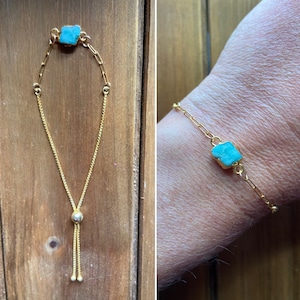 Puede incluir: Un brazalete de cadena dorada con un colgante de piedra turquesa. El brazalete tiene un cierre deslizante ajustable.