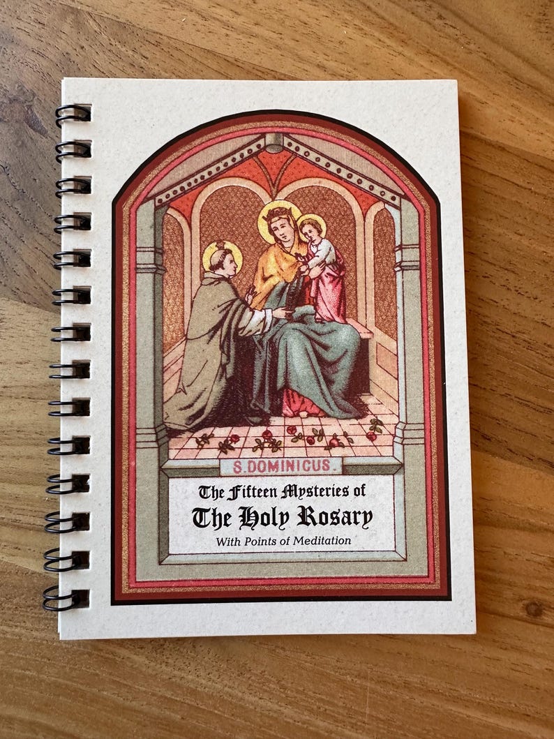 May include: A spiral-bound notebook with a religious illustration on the cover. The artwork depicts figures in robes within an arched frame, with the text "The Fifteen Mysteries of The Holy Rosary" below. The cover has a cream-colored background.