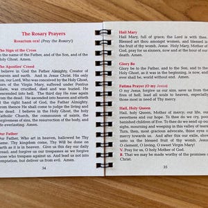 May include: Open booklet with spiral binding, featuring printed text of prayers. The left page displays "The Rosary Prayers" and "The Apostles' Creed." The right page includes "Hail Mary" and "Fatima Prayer." Pages are white with black text.