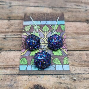 May include: A set of iridescent glitter earrings and a necklace with a hexagonal pendant. The pendant and earrings are filled with blue, purple, red, and green glitter.