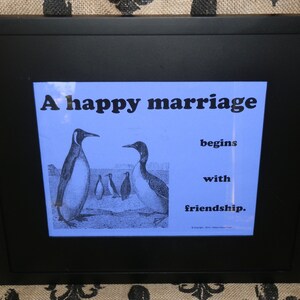 May include: A framed print with a blue background featuring a black and white illustration of penguins. The text reads "A happy marriage begins with friendship."