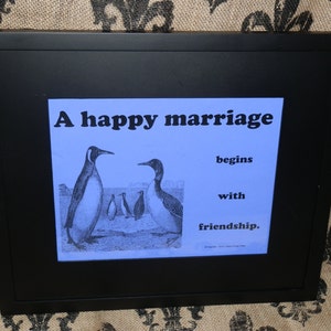 May include: A framed print with a blue background featuring a quote about marriage and penguins. The quote reads "A happy marriage begins with friendship."