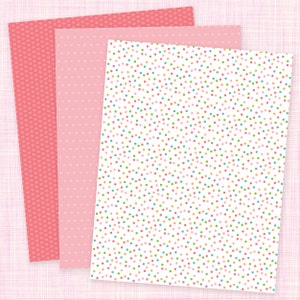May include: Three sheets of patterned paper. The first sheet has a pink background with small red hearts. The second sheet has a pink background with small white dots. The third sheet has a white background with small colorful dots.