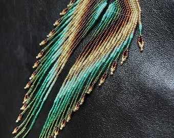 Könnte beinhalten: Ein Paar lange, geperlte Ohrringe mit einem Farbverlauf in Grün, Blau, Braun und Gold. Die Ohrringe sind aus kleinen Perlen gefertigt und haben ein quastenartiges Design.
