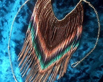 May include: A long, beaded necklace with a fringe design. The necklace is made of brown, pink, green, and purple beads. It has a gold chain attached.