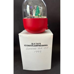 May include: A red and clear plastic snow globe with a miniature ice skater and Christmas tree inside. The base of the globe is red, and the text on the box reads "Ice Skater Jumping Barrel" and "Jumping for Joy 1995."