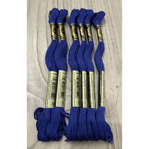 May include: A collection of six skeins of blue embroidery floss. Each skein is wrapped with a paper label and has a metallic gold and black accent. The floss is a vibrant shade of blue.