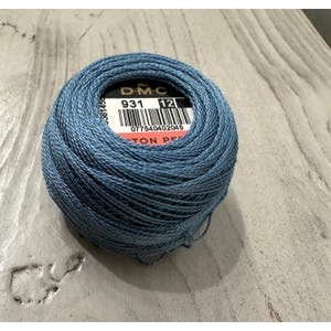 May include: A ball of DMC brand cotton pearl thread in a dusty blue color. The label shows the number 931 and size 12. The thread is tightly wound, and the label is visible on top.