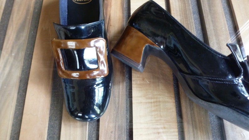 May include: A pair of black patent leather shoes with a brown buckle and a low heel.
