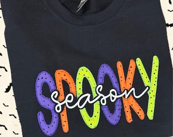 May include: Black sweatshirt with the words "SPOOKY season" embroidered in colorful, dotted letters. The word "season" is in a white cursive font. A sewing machine logo is at the bottom.