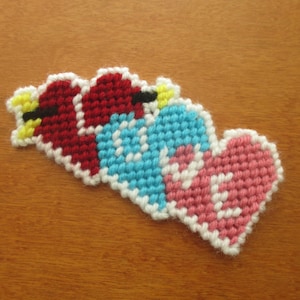 May include: A handmade heart-shaped wall hanging made with colorful yarn in red, white, blue, and pink. The heart is made of individual stitches and has a slightly textured surface.