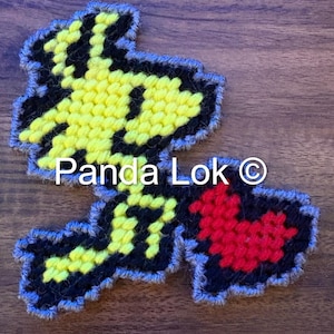 May include: A handmade, pixelated patch featuring a yellow character with black outlines and a red heart. The patch is outlined in gray and has the text "Panda Lok ©".