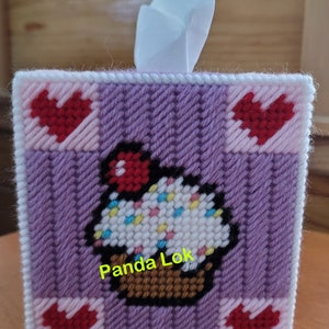 May include: Purple and pink tissue box cover with a white tissue peeking out. The cover has a white cupcake with red and yellow sprinkles and the text "Panda Lok" in green.