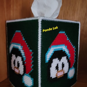 Könnte beinhalten: Ein grüner Taschentuchbox-Bezug mit weißem Rand. Die Vorder- und Rückseite zeigen einen Pinguin mit einer rot-weißen Weihnachtsmütze. Der Text "Panda Lok" ist auf der Seite der Box aufgedruckt.