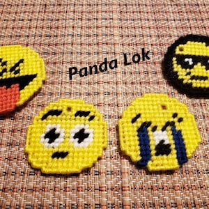 Puede incluir: Cuatro llaveros emoji de fieltro amarillo con diferentes expresiones faciales. Las expresiones incluyen una lengua que sobresale, ojos muy abiertos y llanto. El texto "Panda Lok" es visible en el fondo.