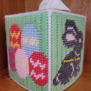 May include: A green crocheted tissue box cover with a black and pink dinosaur on one side and colorful Easter eggs on the other side. The text "Panda Lok" is visible on the dinosaur side.