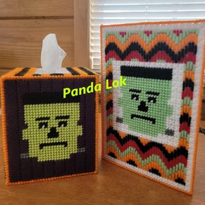 May include: Two handmade tissue box covers featuring a green Frankenstein face. One cover is a square box with a black and orange border. The other cover is a rectangular box with a black, orange, red, and green border.